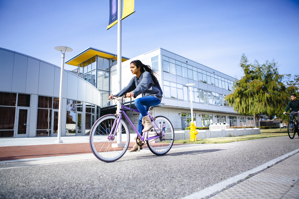 Female student on a bicycle riding along the bike path in front of UC Santa Barbara's Student Resource Building.
