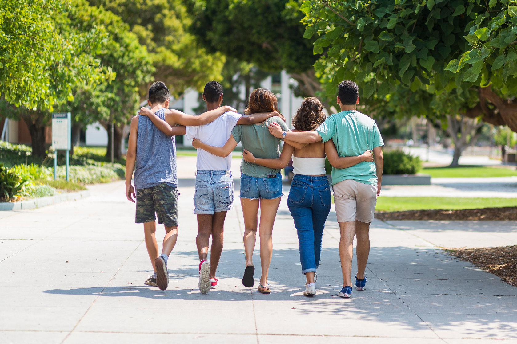 A group of students walks down a path on the UCSB campus with their arms around each others shoulders.